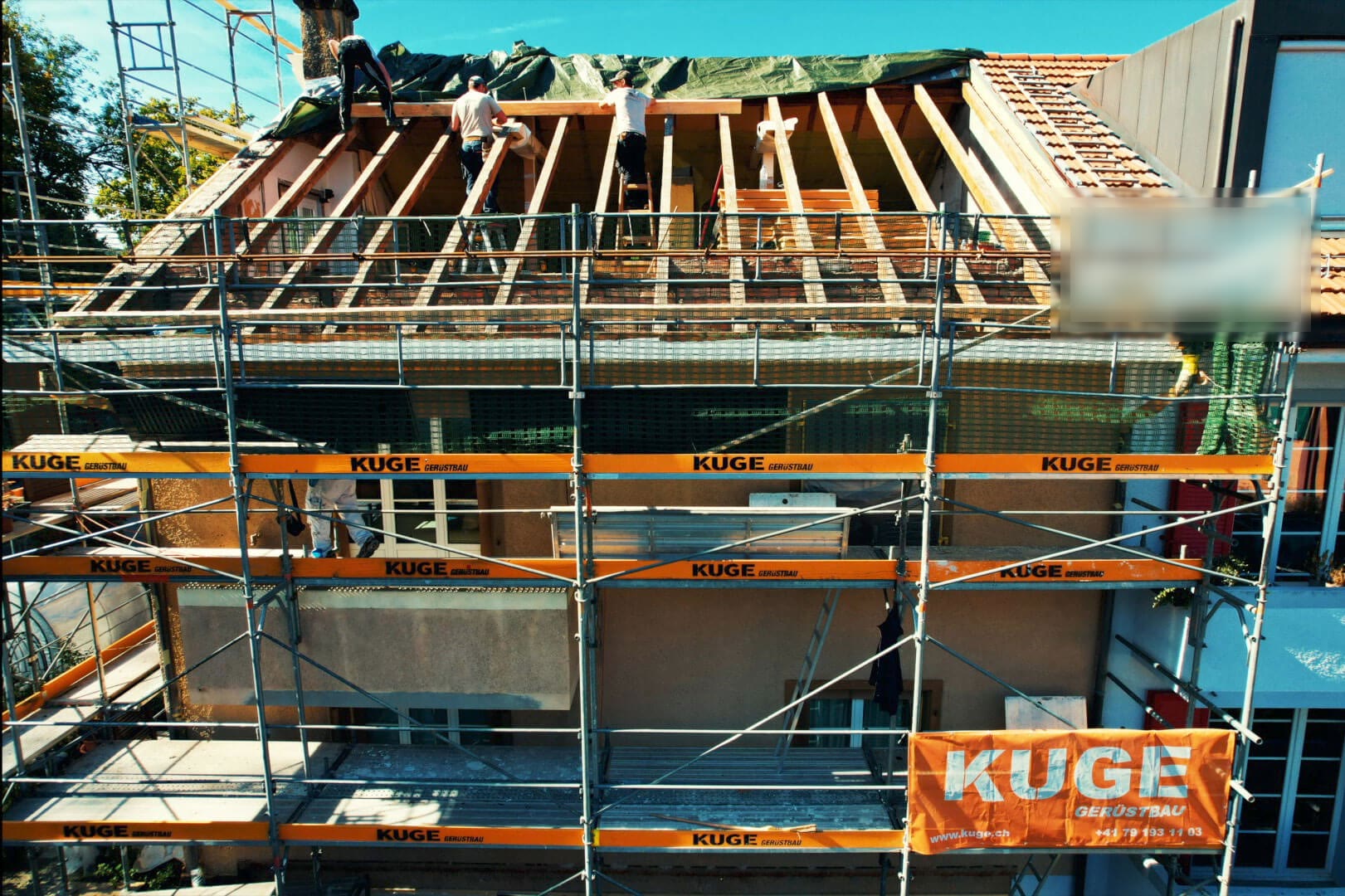 Offener Dachstuhl hinter einem Fassadengerüst, oben mit Abdeckplane geschützt – Foto: KUGE Bau AG